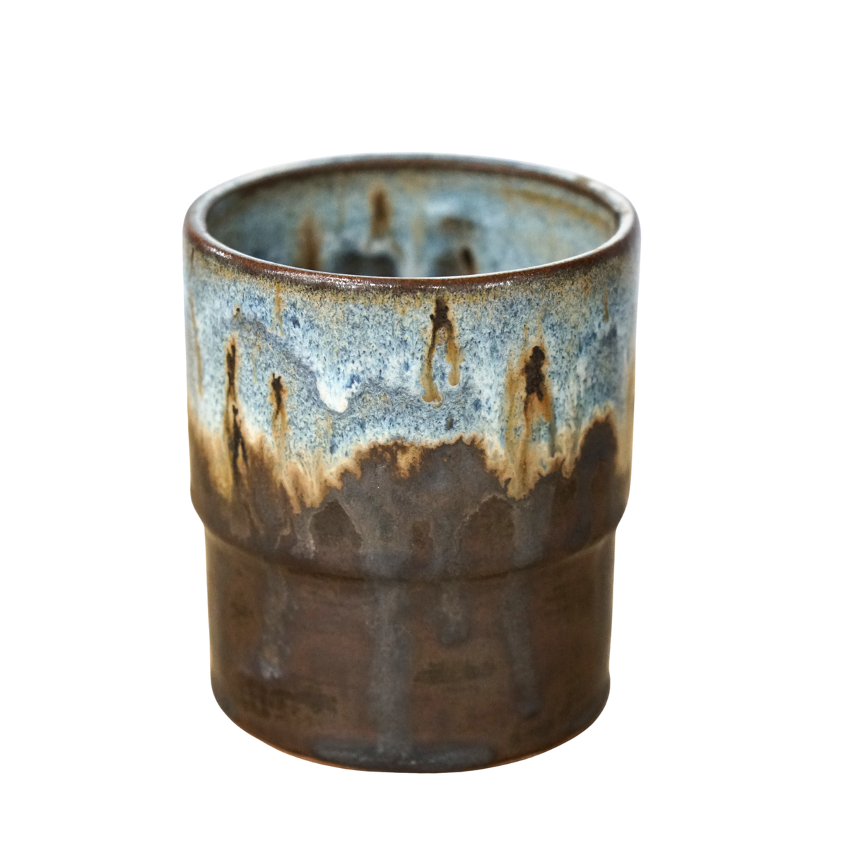 A handmade ceramic cup with a textured, ribbed exterior and a dripping glaze showing shades of brown, blue, and beige on a white background.