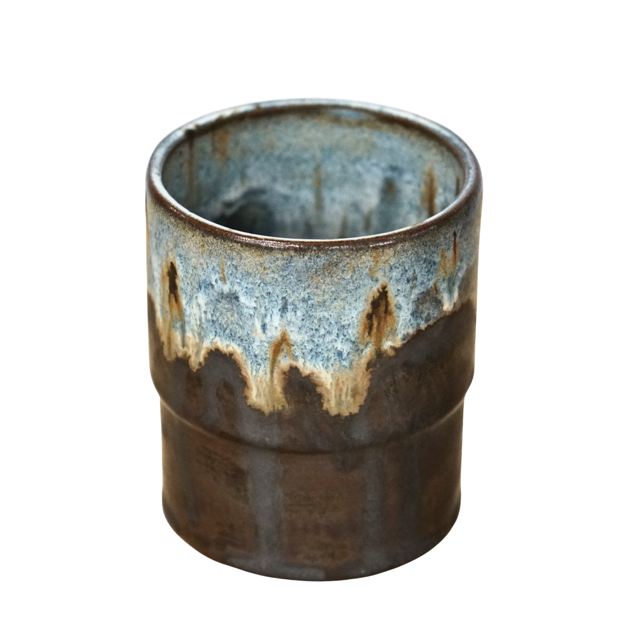 A handmade ceramic cup with a rustic dripping glaze, featuring a dark brown base and a blue-gray top section with brown and beige accents, set against a plain white background.